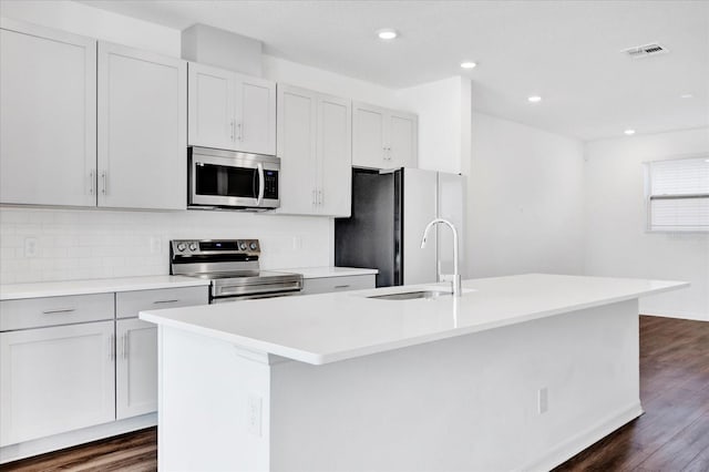 kitchen featuring tasteful backsplash, dark wood finished floors, a center island with sink, stainless steel appliances, and a sink