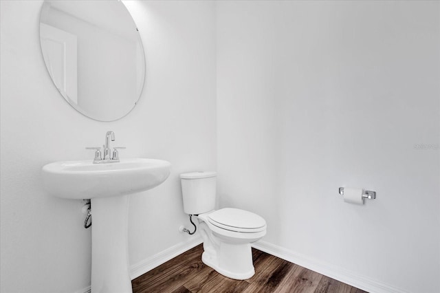 half bathroom with baseboards, toilet, and wood finished floors