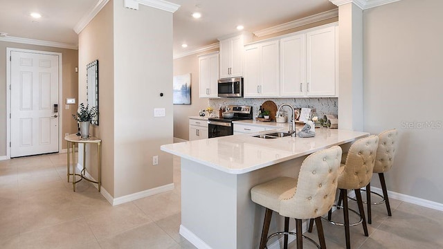 kitchen with sink, appliances with stainless steel finishes, white cabinetry, a kitchen bar, and kitchen peninsula