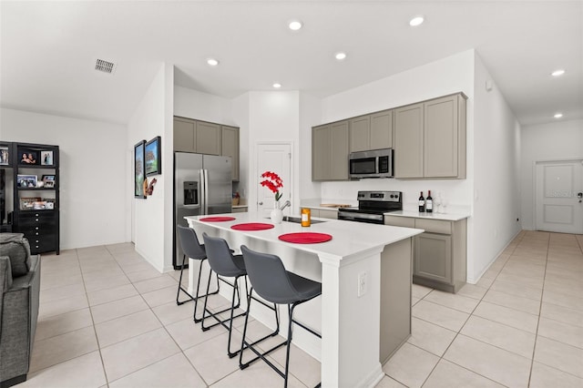 kitchen featuring stainless steel appliances, a kitchen island with sink, a kitchen bar, and gray cabinets