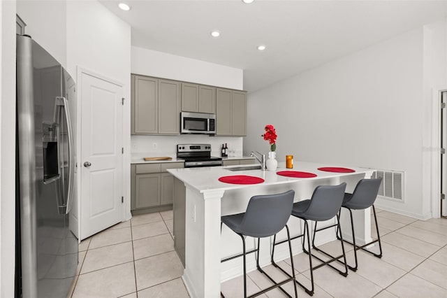 kitchen with sink, a center island with sink, light tile patterned floors, appliances with stainless steel finishes, and a kitchen breakfast bar