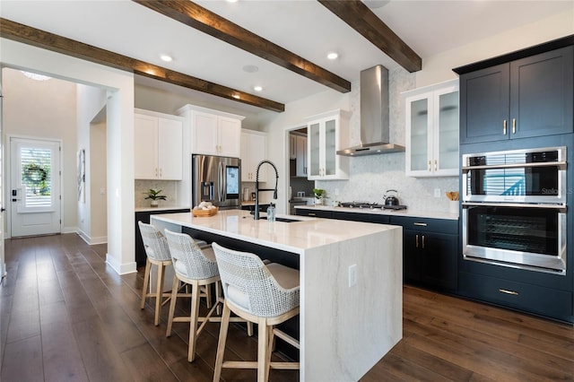 kitchen with wall chimney range hood, sink, a kitchen island with sink, a kitchen breakfast bar, and stainless steel appliances