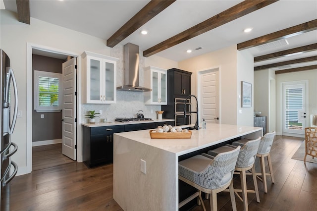 kitchen with tasteful backsplash, a kitchen breakfast bar, stainless steel appliances, a center island with sink, and wall chimney exhaust hood