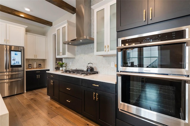 kitchen featuring beamed ceiling, white cabinets, stainless steel appliances, light wood-type flooring, and wall chimney exhaust hood