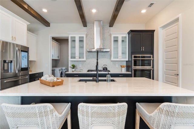 kitchen featuring stainless steel appliances, a large island, washer and clothes dryer, and wall chimney exhaust hood