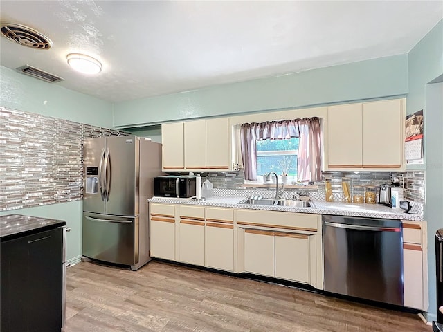 kitchen with tasteful backsplash, sink, stainless steel appliances, and light hardwood / wood-style floors