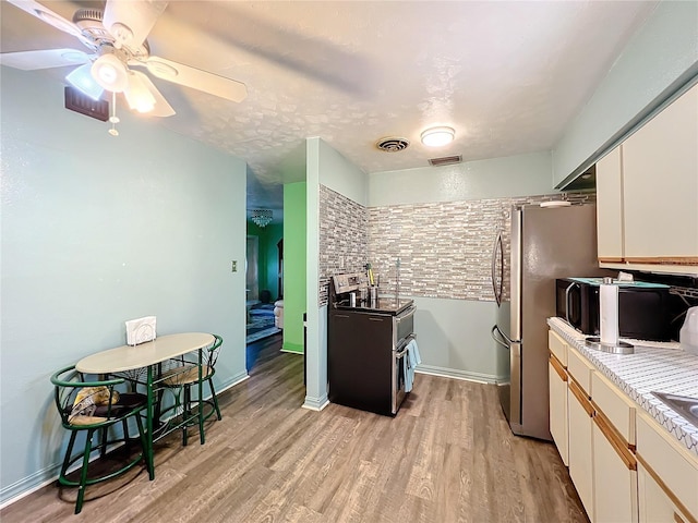 kitchen featuring ceiling fan, stainless steel refrigerator, white cabinets, and light wood-type flooring