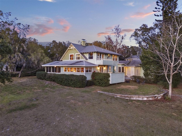 back house at dusk with a balcony and a yard