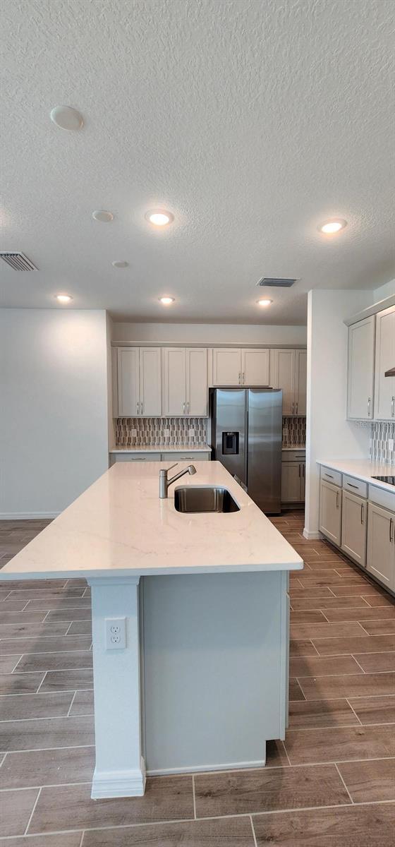 4110 Gooseberry Trl, Kissimmee, FL 34746 - kitchen featuring stainless steel fridge with ice dispenser, wood tiled floors, a sink, an island with sink, and a textured ceiling