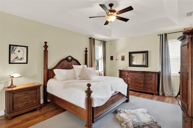 bedroom with hardwood / wood-style flooring, a raised ceiling, and ceiling fan