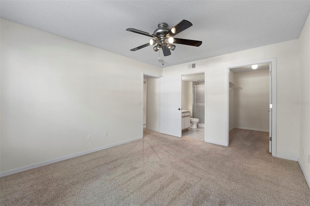 unfurnished bedroom featuring a walk in closet, light colored carpet, a textured ceiling, ensuite bath, and a closet