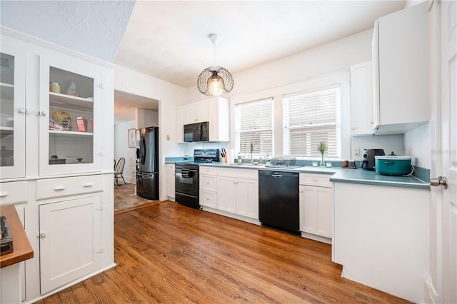 kitchen featuring sink, white cabinets, hanging light fixtures, black appliances, and light hardwood / wood-style flooring