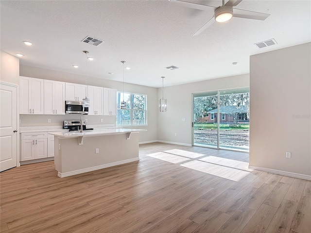 kitchen with light hardwood / wood-style flooring, white cabinetry, hanging light fixtures, a kitchen breakfast bar, and an island with sink