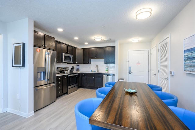 kitchen with appliances with stainless steel finishes, sink, light wood-type flooring, dark brown cabinetry, and a textured ceiling