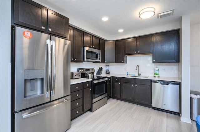 kitchen featuring sink, tasteful backsplash, dark brown cabinets, light wood-type flooring, and appliances with stainless steel finishes