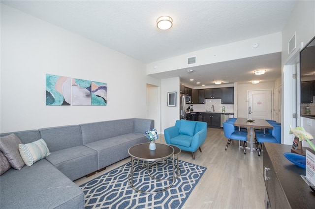 living room featuring sink, a textured ceiling, and light hardwood / wood-style floors