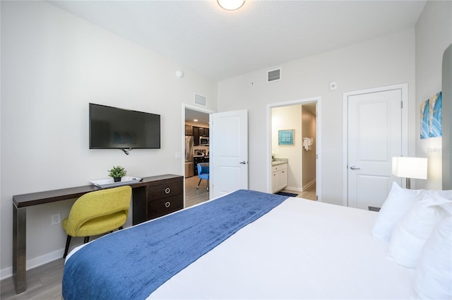 bedroom featuring stainless steel refrigerator, ensuite bath, and light hardwood / wood-style flooring