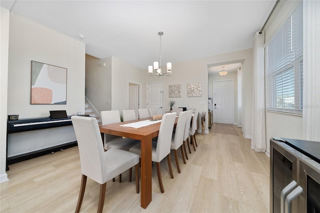 dining space with a notable chandelier, beverage cooler, and light wood-type flooring