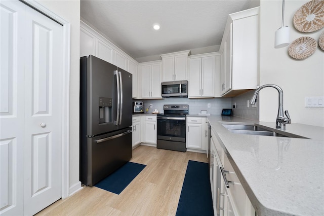 kitchen featuring sink, white cabinetry, hanging light fixtures, stainless steel appliances, and light wood-type flooring