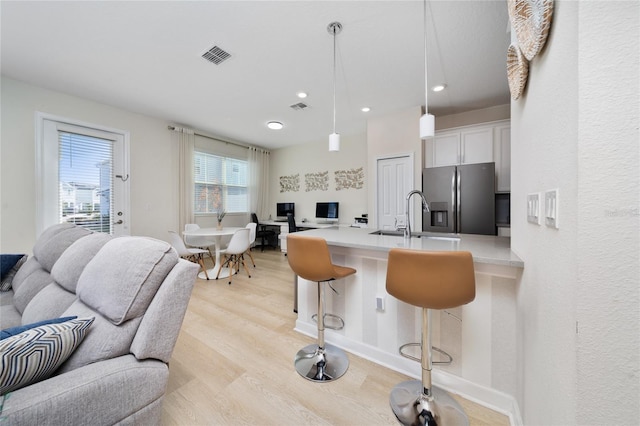 kitchen with sink, stainless steel fridge, a breakfast bar, white cabinetry, and hanging light fixtures