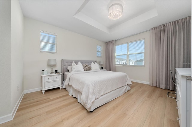 bedroom with an inviting chandelier, light hardwood / wood-style flooring, and a raised ceiling