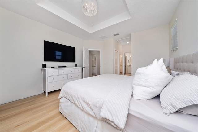 bedroom featuring connected bathroom, a textured ceiling, light hardwood / wood-style flooring, a tray ceiling, and a notable chandelier