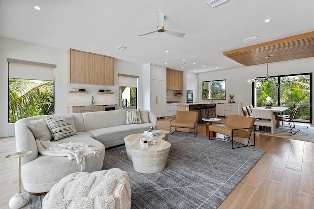 living room with ceiling fan with notable chandelier, light hardwood / wood-style floors, and sink