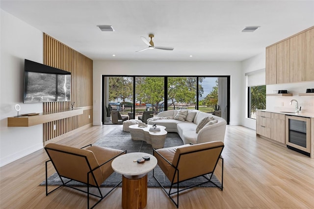 living room with light wood-type flooring, sink, beverage cooler, and ceiling fan