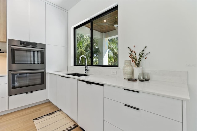 kitchen with white cabinets, double oven, light hardwood / wood-style flooring, and sink