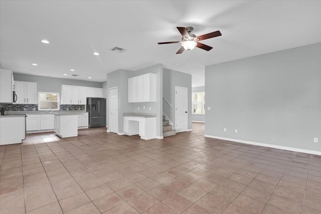 kitchen with light tile patterned floors, backsplash, white cabinets, a kitchen island, and black fridge