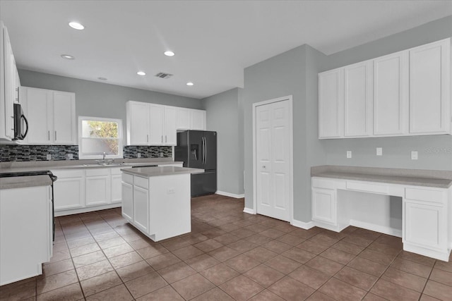 kitchen featuring black appliances, built in desk, a kitchen island, decorative backsplash, and white cabinets