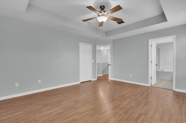 unfurnished bedroom featuring ceiling fan, ensuite bath, a raised ceiling, and light hardwood / wood-style floors