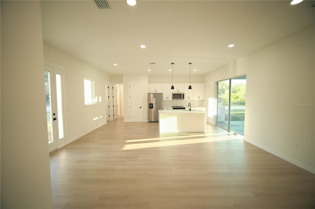 kitchen with white cabinetry, hanging light fixtures, light wood-type flooring, appliances with stainless steel finishes, and a kitchen island with sink