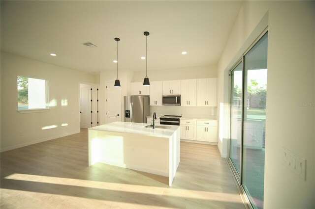 kitchen featuring appliances with stainless steel finishes, a kitchen island with sink, pendant lighting, light hardwood / wood-style floors, and white cabinets