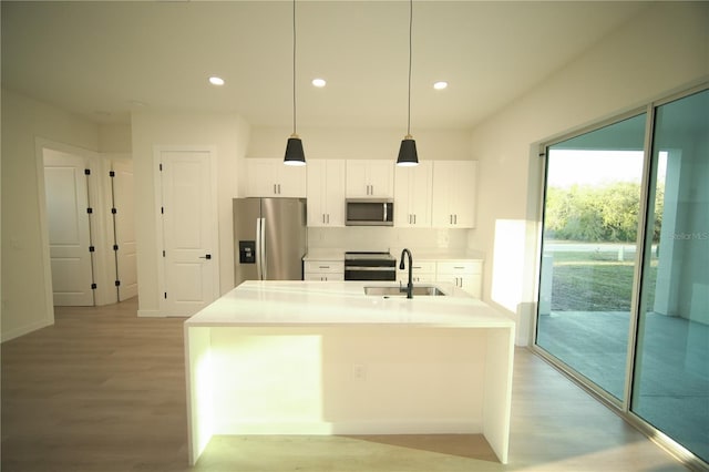 kitchen featuring appliances with stainless steel finishes, a kitchen island with sink, white cabinets, and decorative light fixtures