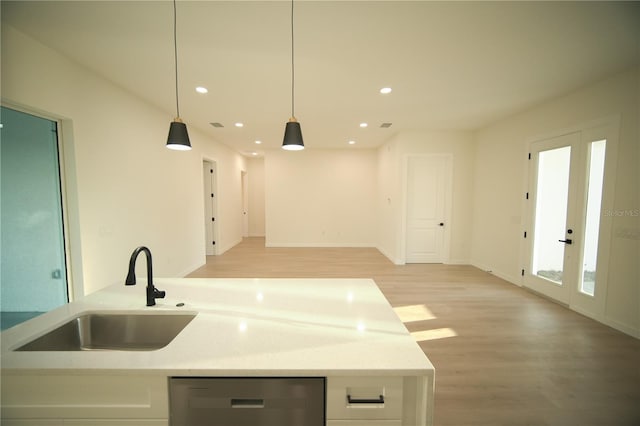 kitchen with pendant lighting, sink, stainless steel dishwasher, light stone counters, and light hardwood / wood-style floors