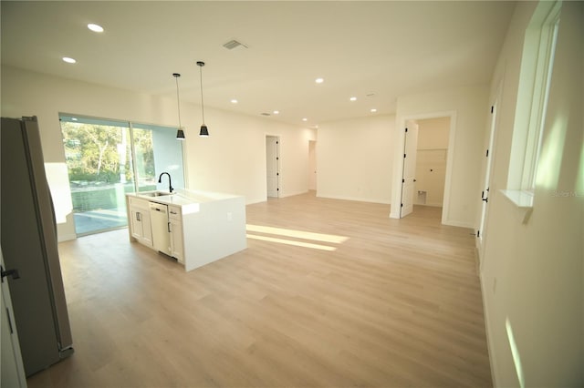 kitchen with dishwashing machine, a kitchen island with sink, hanging light fixtures, fridge, and white cabinets