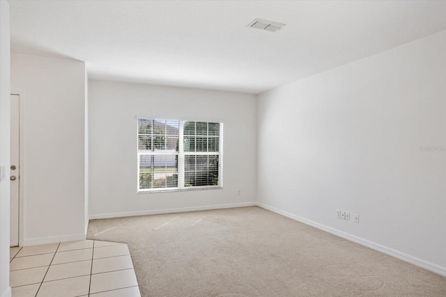 spare room featuring baseboards, visible vents, and light carpet