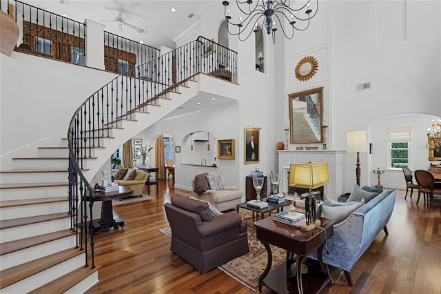 living room featuring ceiling fan with notable chandelier, wood-type flooring, ornamental molding, and a high ceiling