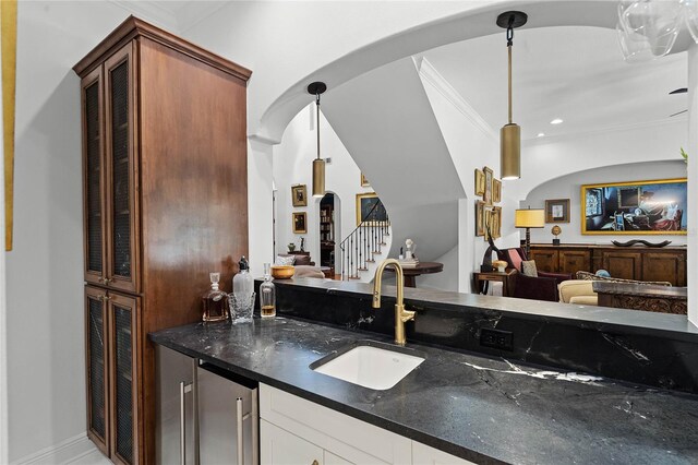 kitchen featuring crown molding, decorative light fixtures, sink, and dark stone countertops