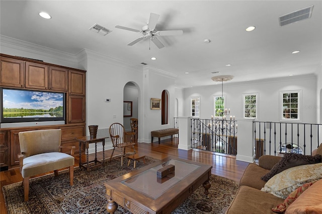 living room with crown molding, dark wood-type flooring, and ceiling fan with notable chandelier