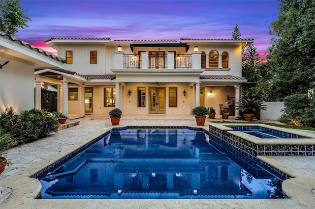 back house at dusk featuring a pool with hot tub, ceiling fan, a patio, and a balcony