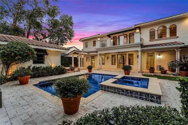 back house at dusk with a swimming pool with hot tub, ceiling fan, a patio, and a balcony