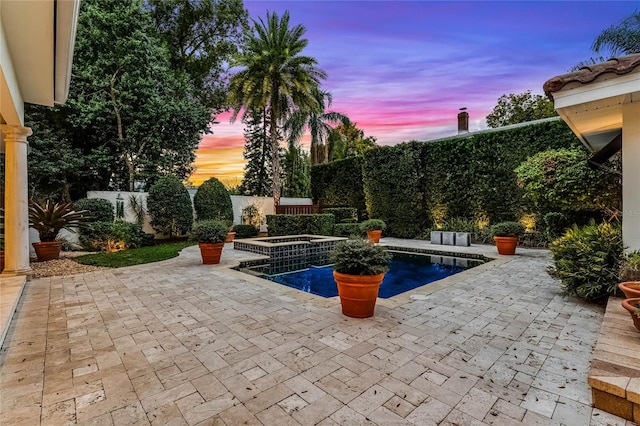 pool at dusk featuring an in ground hot tub and a patio area