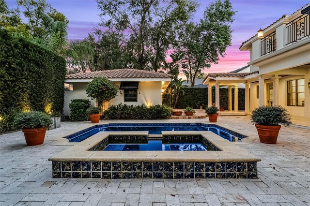 pool at dusk featuring an in ground hot tub and a patio area