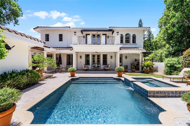 back of house with french doors, a balcony, a swimming pool with hot tub, and a patio