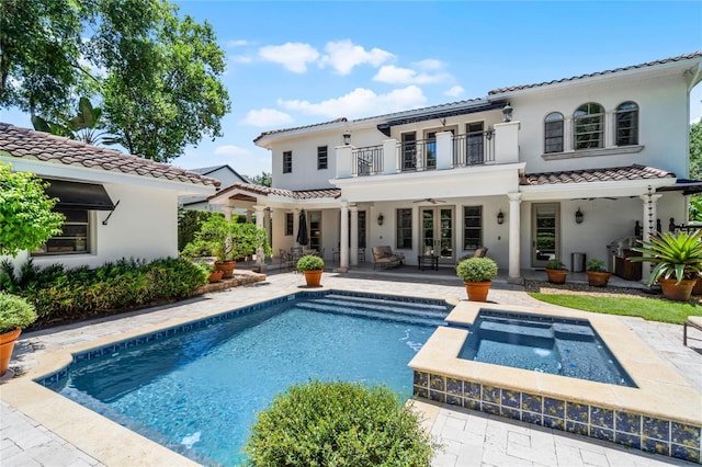 rear view of house with a swimming pool with hot tub, ceiling fan, a patio, and a balcony