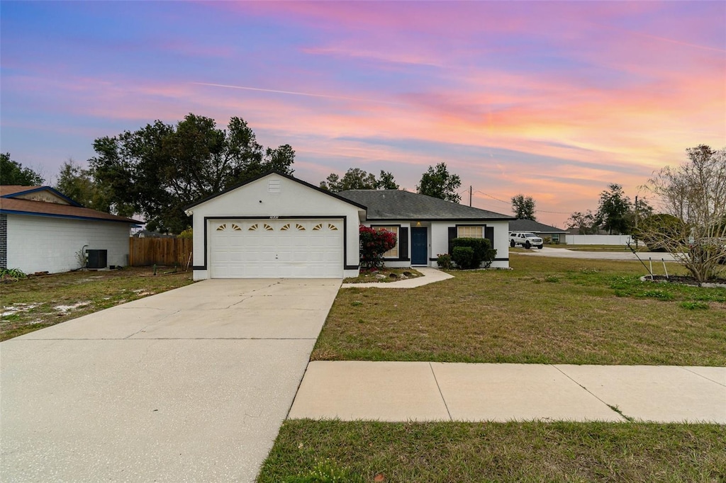 ranch-style home featuring a garage, central AC unit, and a lawn