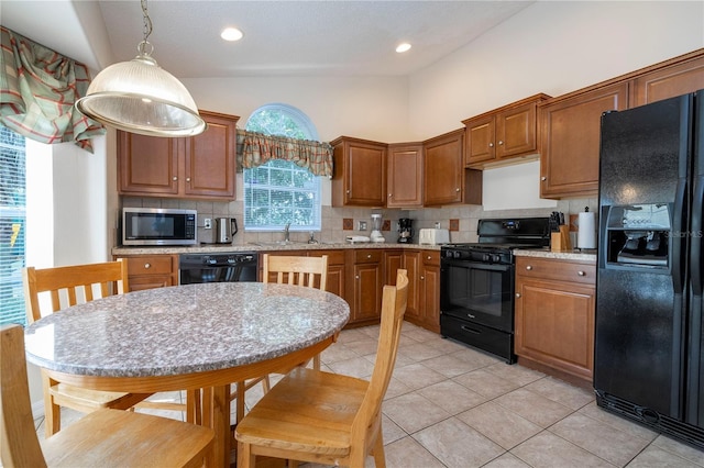 kitchen featuring hanging light fixtures, light stone countertops, backsplash, and black appliances