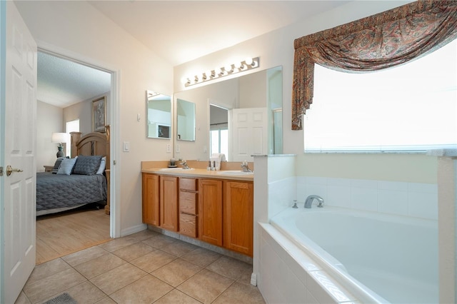 bathroom with tile patterned flooring, tiled tub, vanity, and lofted ceiling